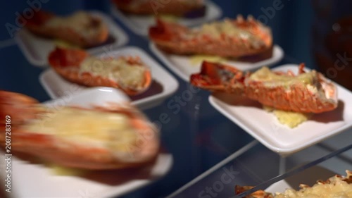 Close-up, shallow depth-of-field (shallow DoF) tracking shot of a buffet station showcasing multiple perfectly plated gourmet lobster tails au gratin.