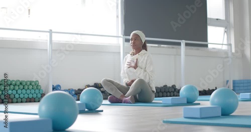Hooded woman settling, placing hands on chest, belly, guiding breath on blue mat in studio calming