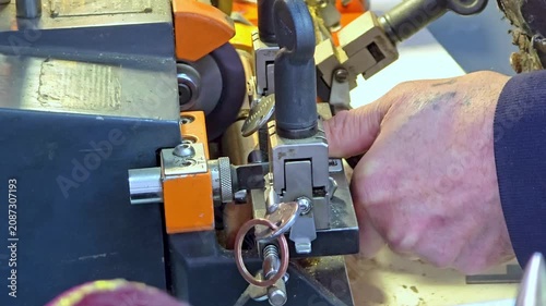 Hand operating key cutting machine in workshop, metal components visible