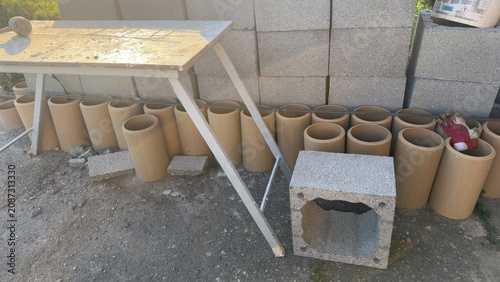 Construction site with concrete blocks and pipes ready for work. Metal worktable placed in front of stacked blocks. Scene shows early morning light on gravel and greenery