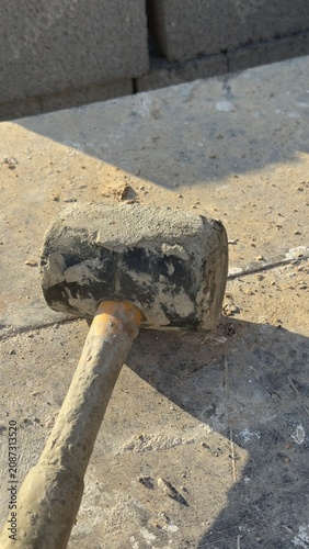 Worn rubber mallet rests on dusty concrete ground. Tool shows signs of heavy use. Ideal for construction, DIY, or repair themed content. Suggests manual labor or home improvement projects