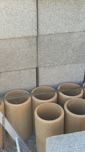 Stacked concrete blocks and cylindrical pipes in construction zone. Neat rows show building materials ready for use. Image captures industrial site with raw textures and practical setup