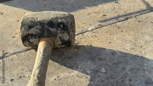 Worn rubber mallet rests on dusty concrete ground. Tool shows signs of heavy use. Ideal for construction, DIY, or repair themed content. Suggests manual labor or home improvement projects