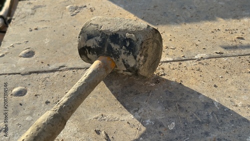Worn rubber mallet rests on dusty concrete ground. Tool shows signs of heavy use. Ideal for construction, DIY, or repair themed content. Suggests manual labor or home improvement projects