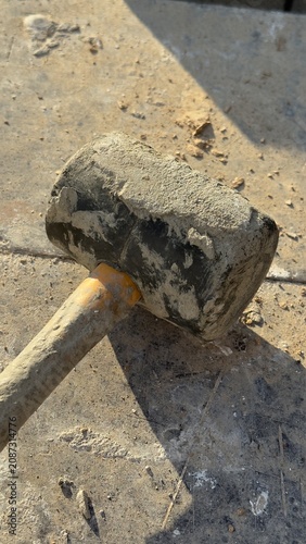 Worn rubber mallet rests on dusty concrete ground. Tool shows signs of heavy use. Ideal for construction, DIY, or repair themed content. Suggests manual labor or home improvement projects