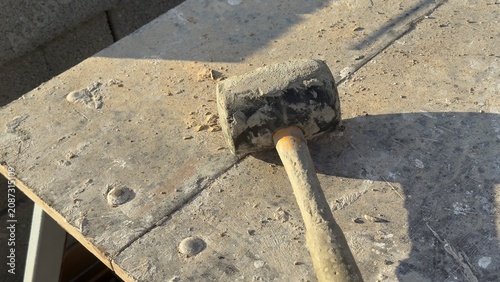 Worn rubber mallet rests on dusty concrete ground. Tool shows signs of heavy use. Ideal for construction, DIY, or repair themed content. Suggests manual labor or home improvement projects