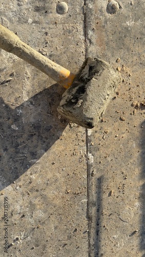 Worn rubber mallet rests on dusty concrete ground. Tool shows signs of heavy use. Ideal for construction, DIY, or repair themed content. Suggests manual labor or home improvement projects