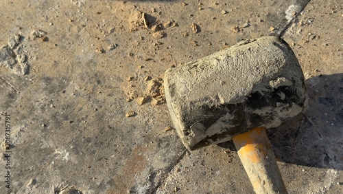 Worn rubber mallet rests on dusty concrete ground. Tool shows signs of heavy use. Ideal for construction, DIY, or repair themed content. Suggests manual labor or home improvement projects