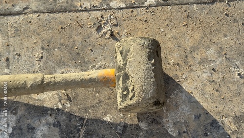 Worn rubber mallet rests on dusty concrete ground. Tool shows signs of heavy use. Ideal for construction, DIY, or repair themed content. Suggests manual labor or home improvement projects