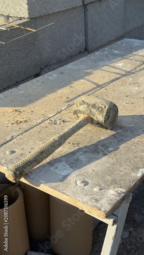 Worn rubber mallet rests on dusty concrete ground. Tool shows signs of heavy use. Ideal for construction, DIY, or repair themed content. Suggests manual labor or home improvement projects