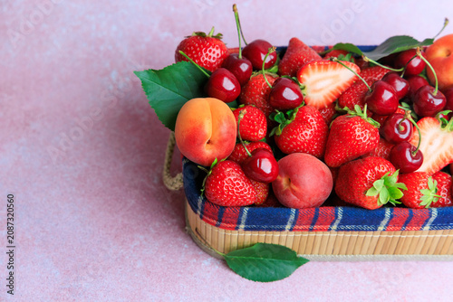 apricot, cherry, strawberry fruits in a basket with strawberries cherries and apricots on a pink background