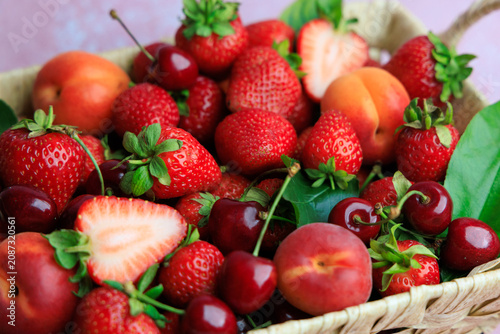 Fresh fruit basket with strawberries cherries and peaches on a pink background in a sunny kitchen setting during daytime