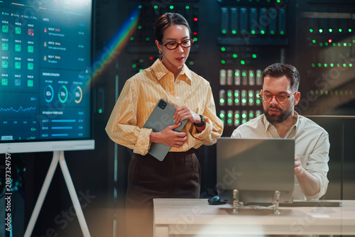 It engineers collaborating on network infrastructure planning in a modern data center server room with data screens
