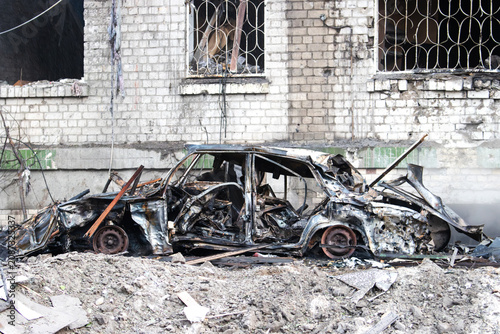 Tableau sur toile Completely incinerated car wreckage abandoned in front of a ruined building