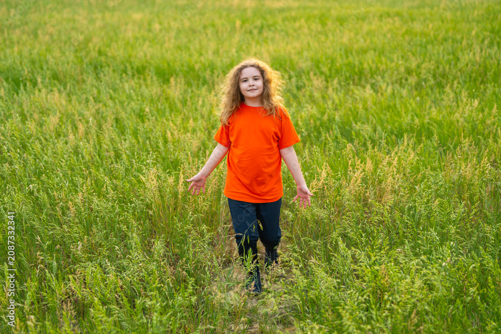 Naklejka premium Kid on grass field. Grass meadow creates fresh green background. Child walks through grass outdoors. Summer landscape shows grass freedom lifestyle.