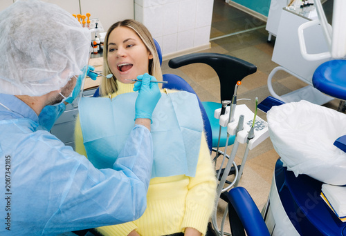 A male dentist with dental tools drills the teeth of a patient with an assistant. The concept of medicine, dentistry and healthcare