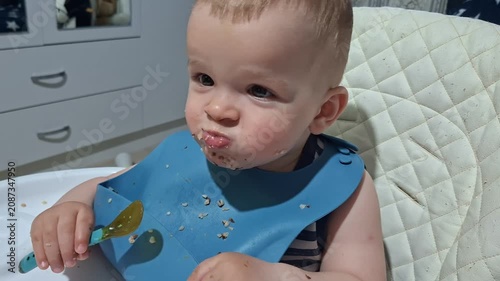 Adorable messy baby eating oatmeal in high chair