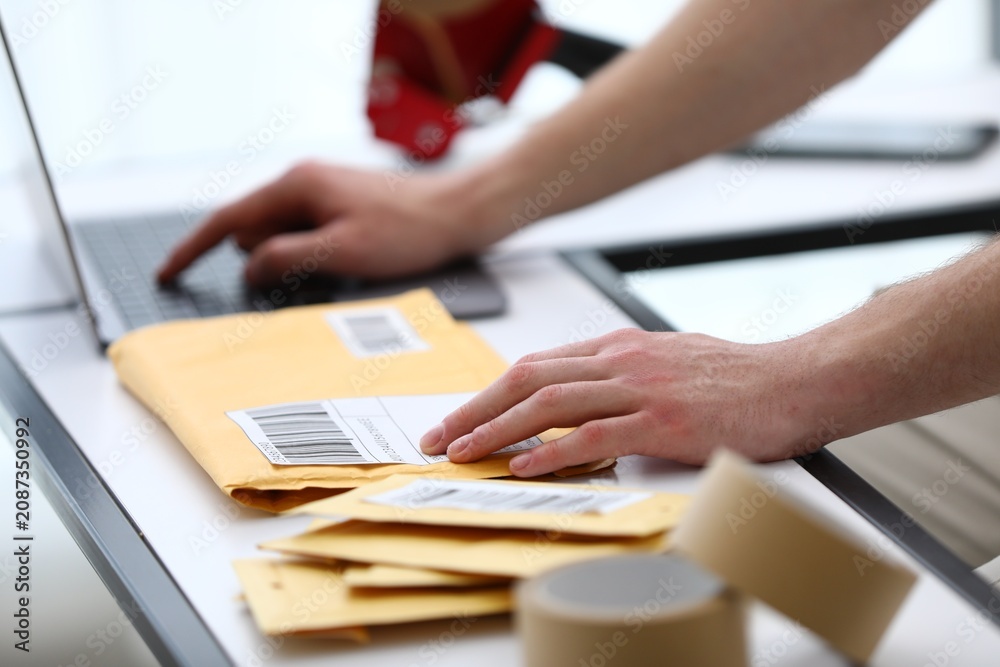 Fototapeta premium Man with postal envelopes working on laptop at table in office, closeup