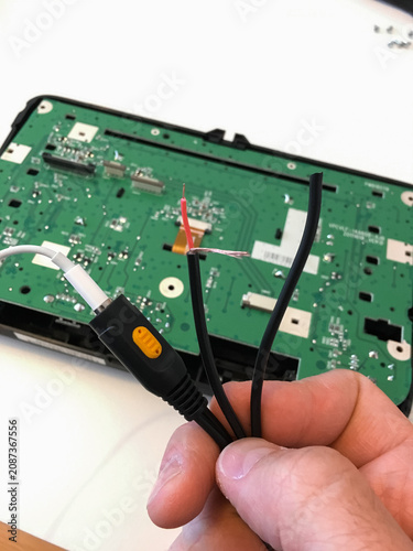 Hand holding a black connector and cables near the green circuit board of a car radio.