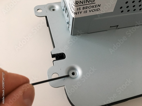 Hand using a black tool on the metal casing of a car radio during disassembly.