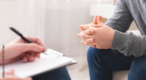 Fotografie Therapist writing notes during counseling session with single man sitting on cou