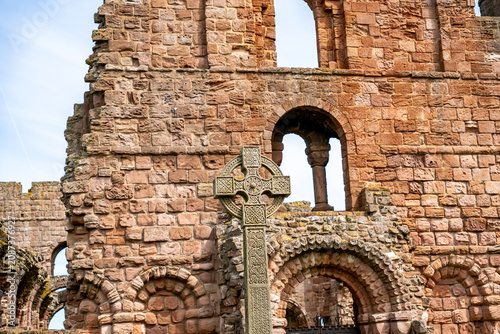 An ornate Celtic cross stands outside the historic abbey ruins, its intricate carvings and timeless design reflecting centuries of faith, craftsmanship and heritage.