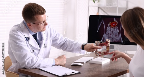 Foto Gastroenterologist showing model of large intestine to patient at desk in clinic