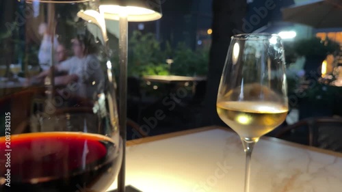 relaxed evening dining experience with wine glasses and ambient lighting in an outdoor area at night with people in the background, slightly elevated perspective.