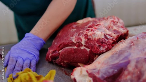 Market vendor cleaning butcher counter and preparing large beef rib roast with knife for cutting and selling fresh meat at traditional local market