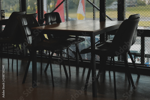 Obraz na plátně A simple setting with a wooden table and black chairs situated in front of a win