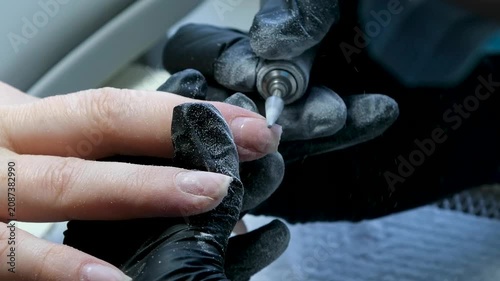 Close up professional manicure by female nail technician wearing glasses yellow shirt and black latex gloves providing careful nail treatment for woman in modern beauty salon