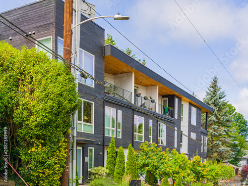 Modern dark grey apartment building with wooden balcony and greenery