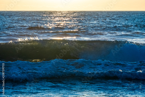 Breaking ocean wave with white foam crest at golden hour on Santa Monica Beach, Pacific Ocean, California, USA.