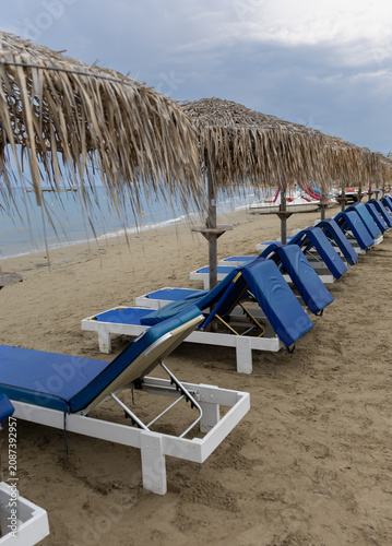 Photos Row of empty blue sunbeds and straw umbrellas on a sandy beach under a cloudy sky