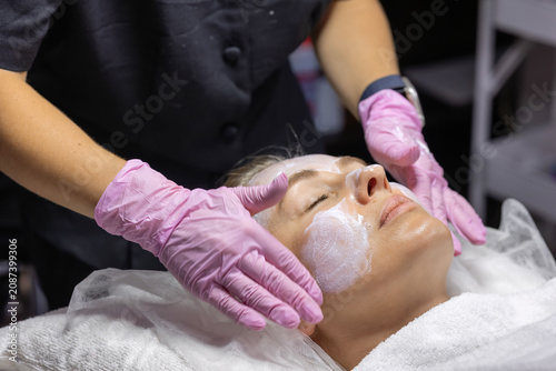 Fotografie Cosmetologist applies a nourishing facial cream with gentle massage movements during a professional skincare treatment to hydrate, soothe and protect the skin