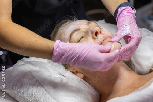 Professional cosmetologist gently massages a woman's face while applying moisturizing skincare cream during a facial treatment for hydration, relaxation, glowing skin and beauty care.