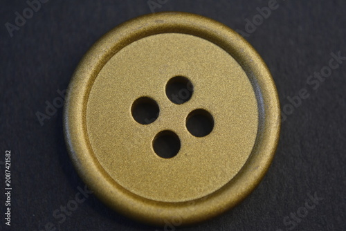 Foto Round gold button with four holes on a dark background