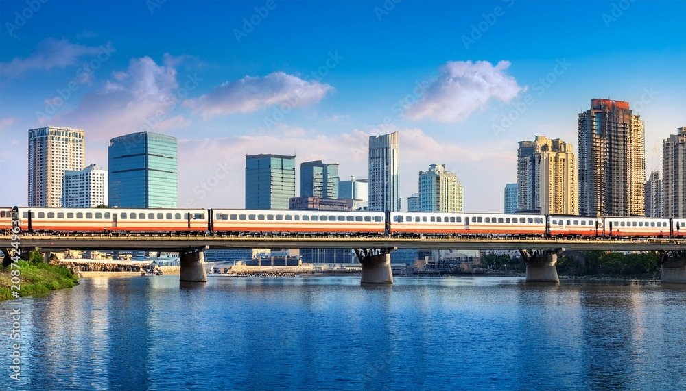 Obraz premium train traveling along river with city skyline background