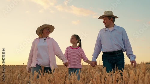 Father mother, child girl walk hand in hand in wheat field. Happy family farmers with child stroll wheat field. Dad mom, young daughter farmers enjoy outdoors together. Family business. Slow motion