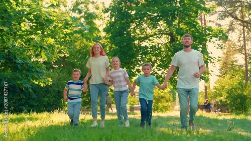 Parents, father mother, children son daughter play together grass in park summer. Happy family runs green lawn. Dad mom, kids son daughter walk in outdoors. Family picnic with children. Slow motion