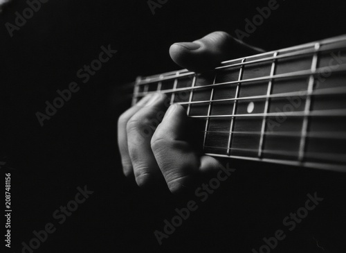 Close-up of a hand playing an acoustic guitar in black and white with dramatic lighting