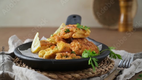 Golden crispy cod fish fritters arranged on a rustic black skillet with lemon wedges and fresh parsley, captured with soft, warm studio lighting that accentuates the appetizing texture.