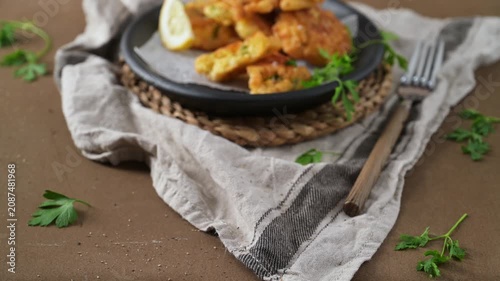 A close-up shot capturing a delicious stack of crispy, golden cod fish fritters in a rustic black skillet. The dish is garnished with fresh parsley and lemon wedges, resting on a textured linen cloth 