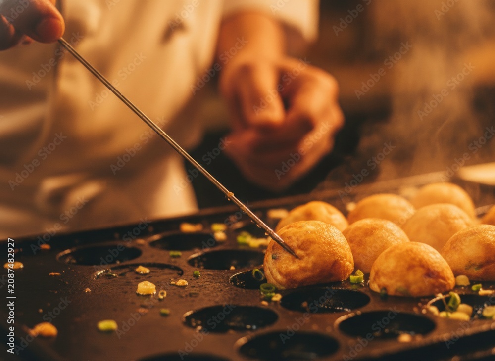 Fototapeta premium Chef Preparing Takoyaki Balls on Hot Griddle with Steam in Warm Lighting