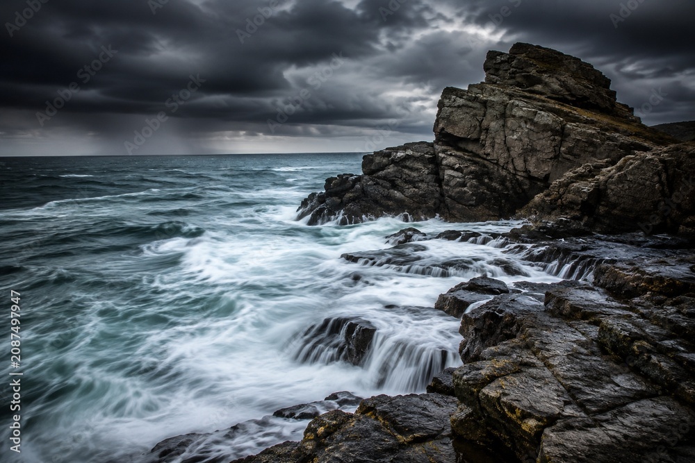 Fototapeta premium Ocean waves crashing against coastal rocks with long exposure motion.
