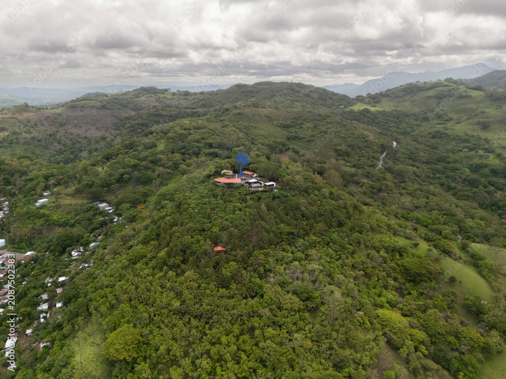 Naklejka premium View of a green hill with buildings and trees under a cloudy sky