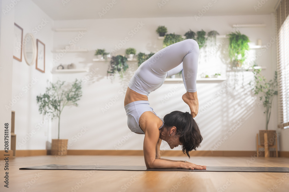 Obraz premium Focused woman practices advanced yoga pose showcasing physical balance strength and flexibility inside serene studio promoting fitness healthy lifestyle wellness and meditation