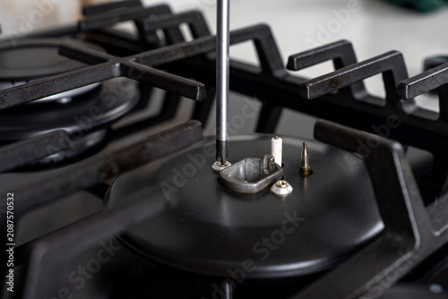 Canvastavla Close-up of a technician unscrewing a fastening bolt on a gas stove burner base using a phillips screwdriver, performing maintenance or disassembly of a domestic kitchen appliance