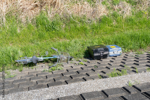 河原の土手に捨てられた不法投棄された旅行ケースと自転車
