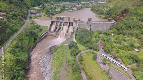 Drone view of a hydroelectric dam surrounded by vibrant greenery, river landscapes, and the natural beauty of Baños, Ecuador.